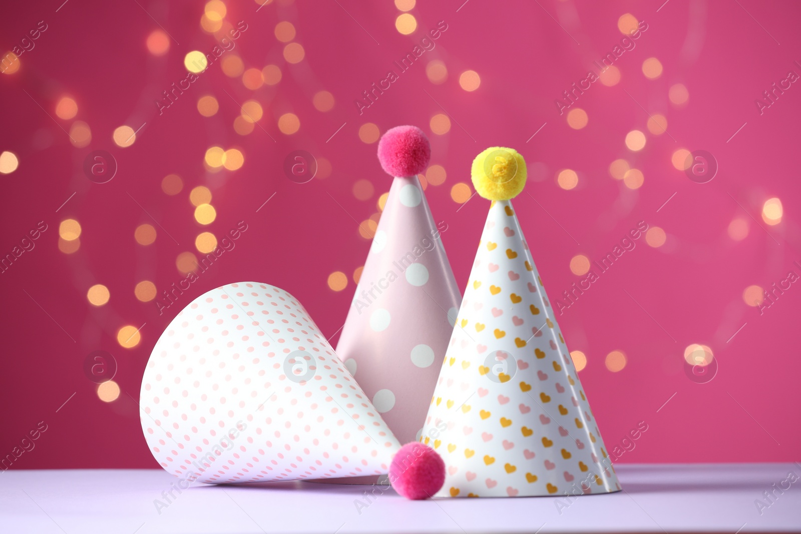 Photo of Party hats on violet table against pink background with blurred lights