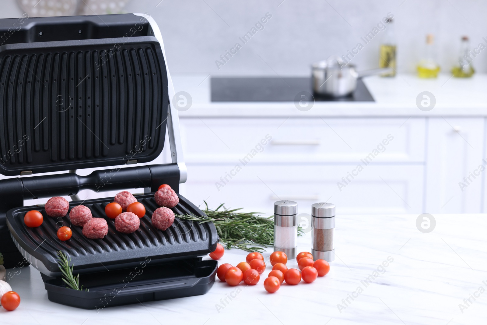 Photo of Electric grill with meatballs, tomatoes, spices and vegetables on white marble table in kitchen. Space for text