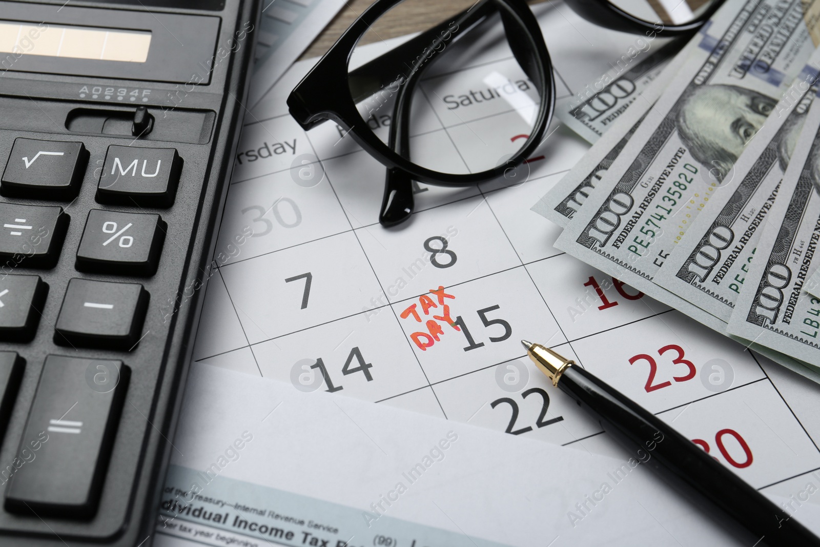 Photo of Calendar with date reminder about tax day, documents, money, pen, calculator and glasses on table, closeup