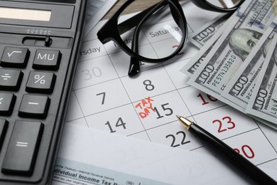 Photo of Calendar with date reminder about tax day, documents, money, pen, calculator and glasses on table, closeup