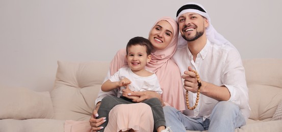 Happy Muslim family spending time together on sofa at home, space for text. Banner design 