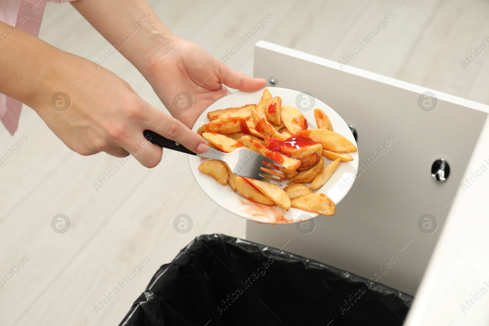 Photo of Woman throwing baked potato with ketchup into bin indoors, closeup