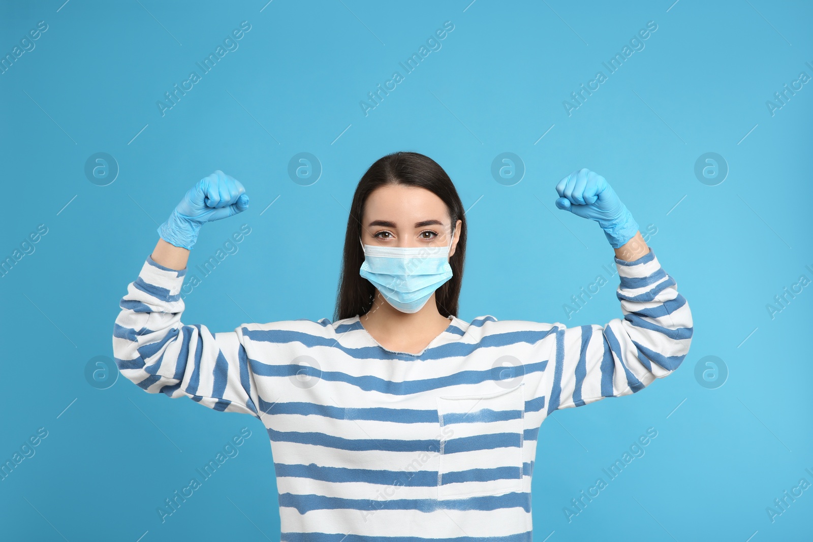 Photo of Woman with protective mask and gloves showing muscles on light blue background. Strong immunity concept