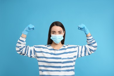 Woman with protective mask and gloves showing muscles on light blue background. Strong immunity concept