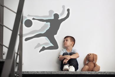 Image of Little boy with soft toy dreaming to be soccer player. Silhouette of man behind kid's back