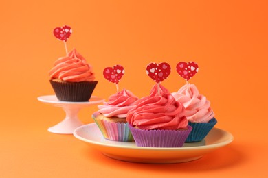Photo of Delicious cupcakes with bright cream and heart toppers on orange background