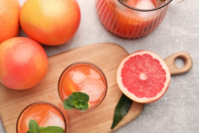 Photo of Tasty freshly made grapefruit juice, fruits and mint on light grey table, flat lay