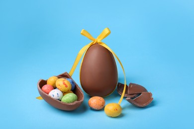 Photo of Tasty whole chocolate eggs with yellow bow and different candies on light blue background