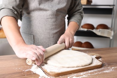 Man rolling dough at table in kitchen, closeup