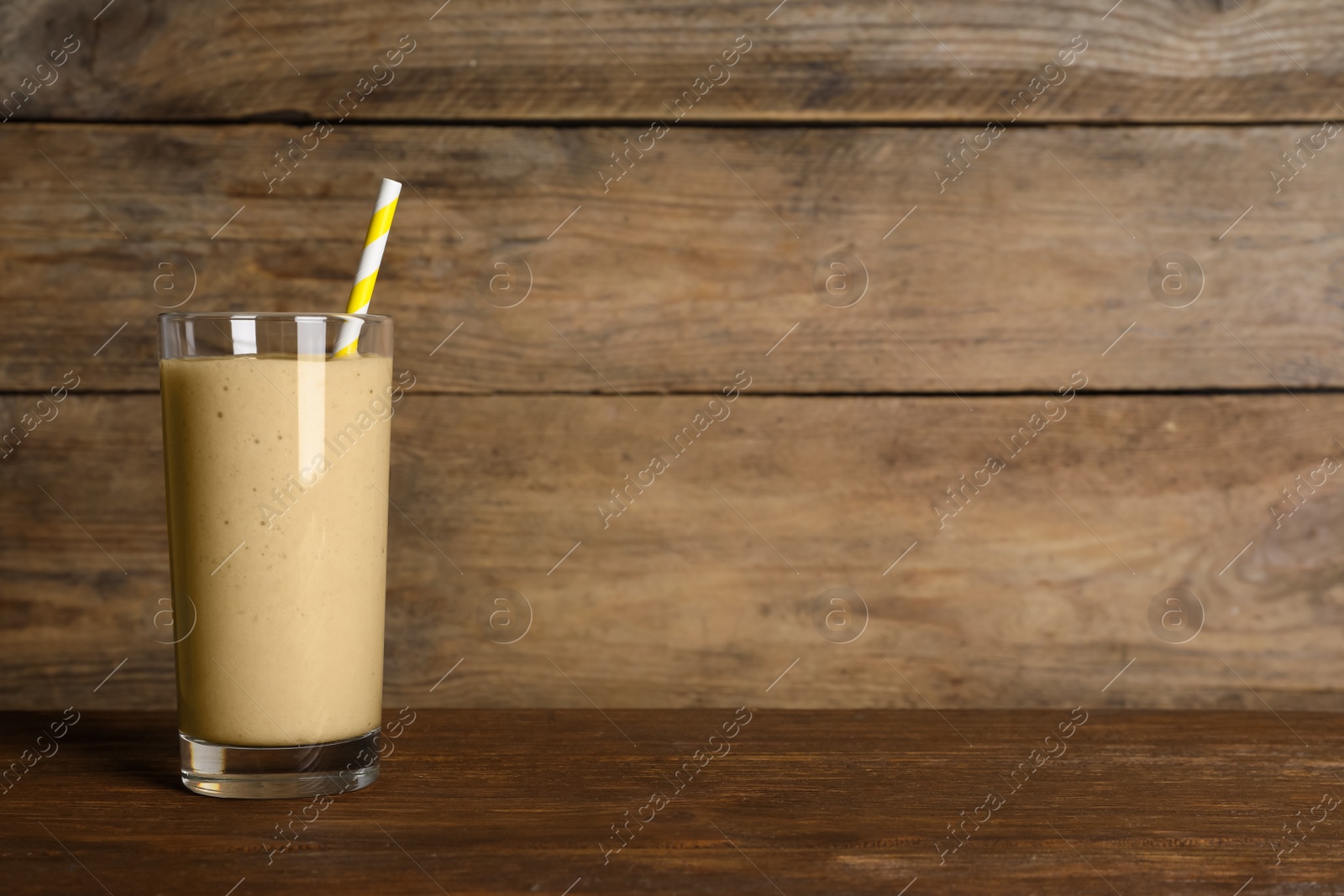 Photo of Glass of tasty smoothie with straw on wooden table. Space for text