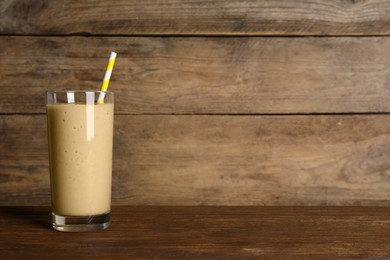 Photo of Glass of tasty smoothie with straw on wooden table. Space for text