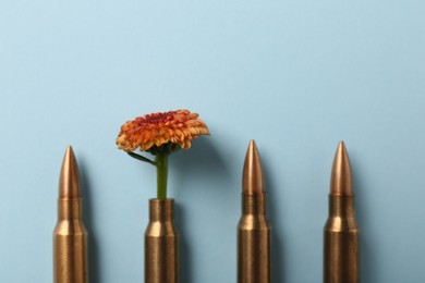 Photo of Bullets and cartridge case with beautiful flower on light blue background, flat lay
