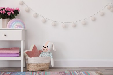 Photo of Stand with houseplant and toys near light wall in baby room. Interior design