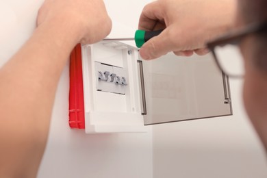 Photo of Electrician with screwdriver installing switchboard on wall indoors, closeup