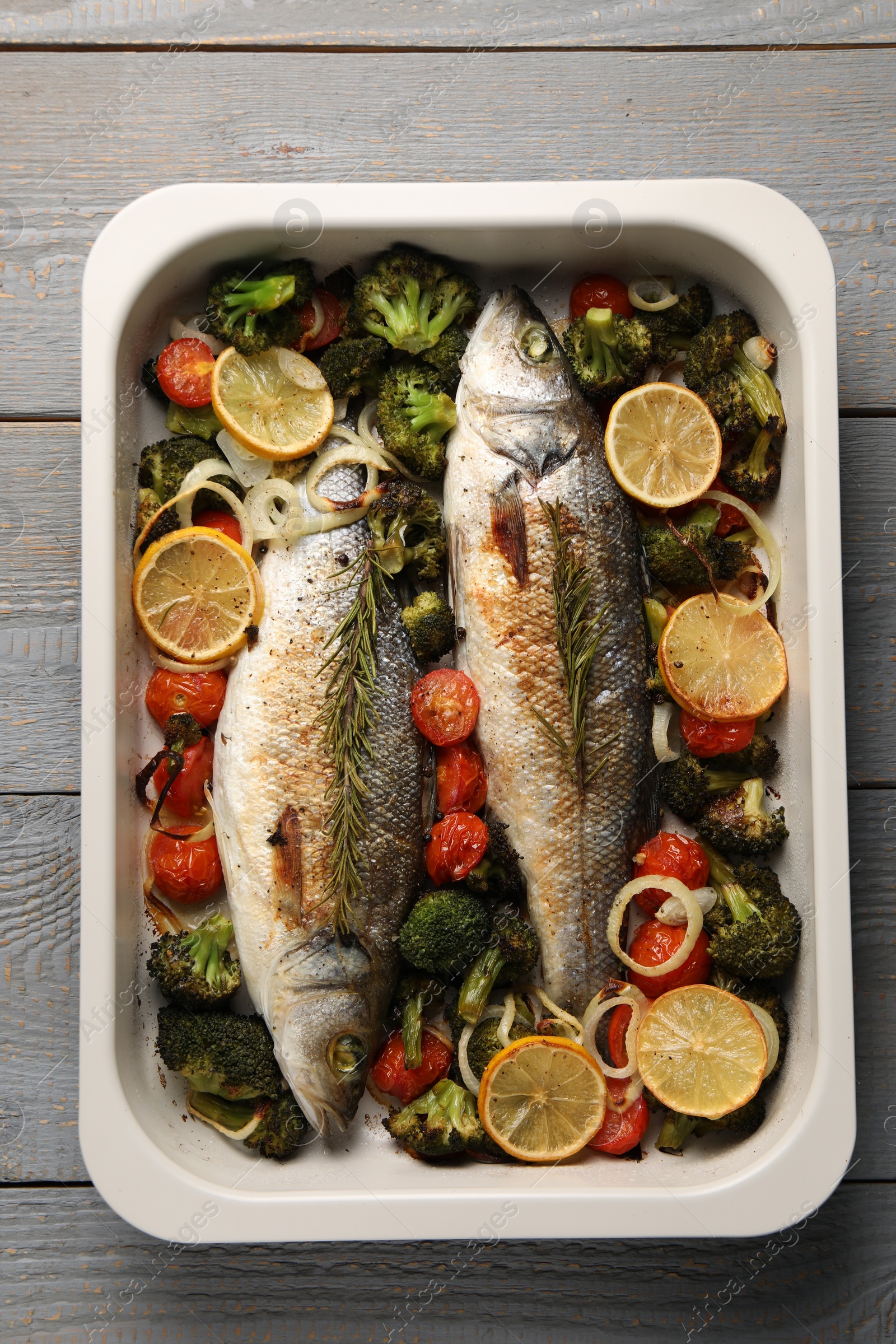 Photo of Delicious fish with vegetables and lemon in baking dish on grey wooden table, top view