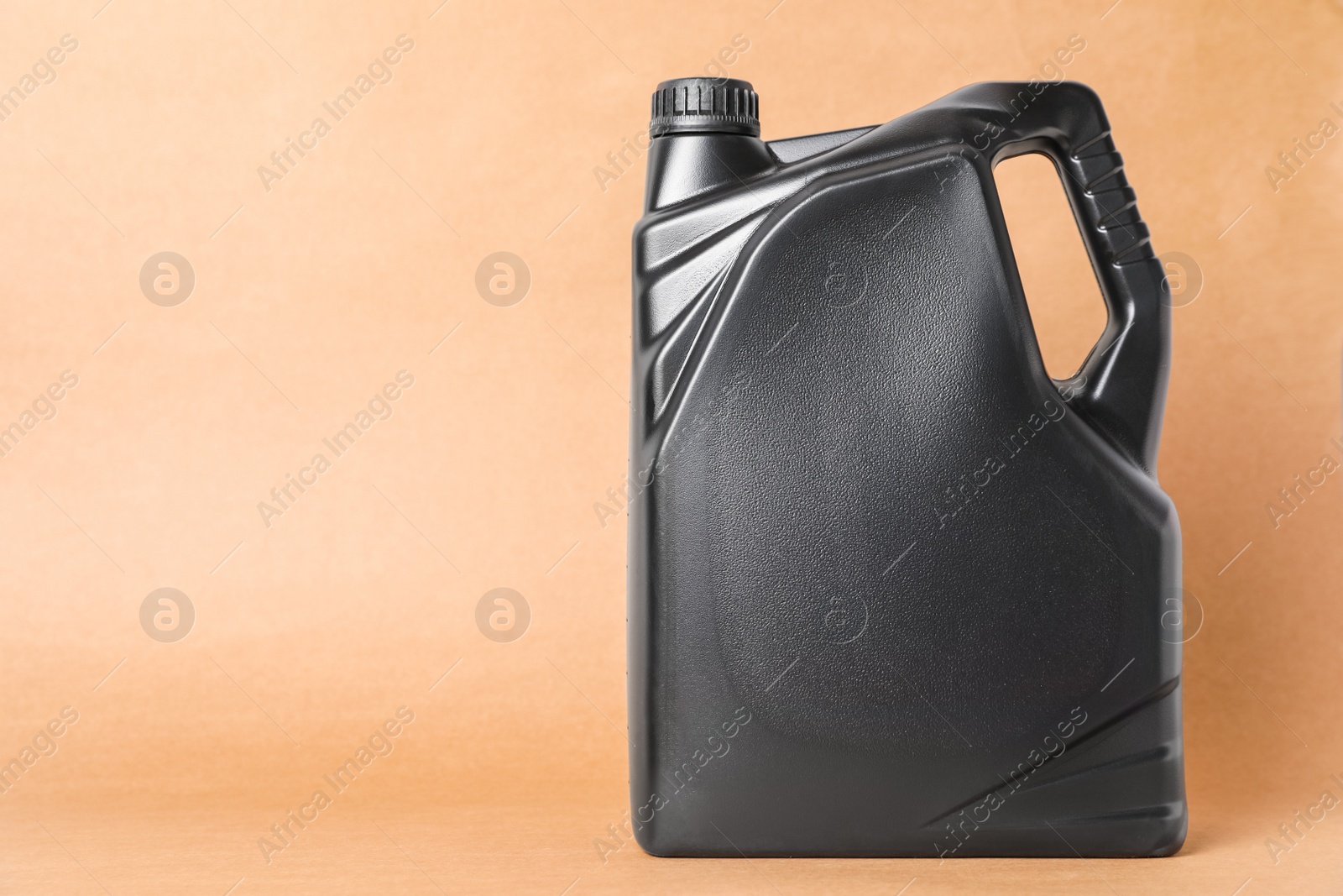 Photo of Motor oil in black canister on light brown background, space for text