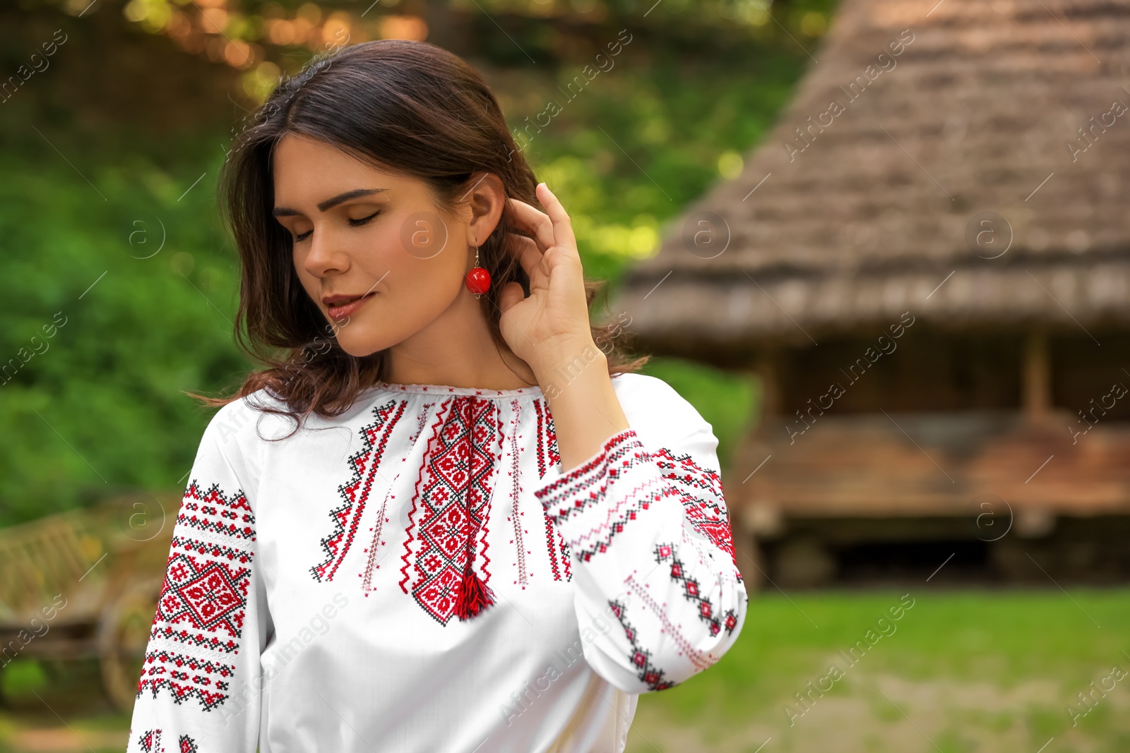 Photo of Beautiful woman wearing embroidered shirt in village, space for text. Ukrainian national clothes