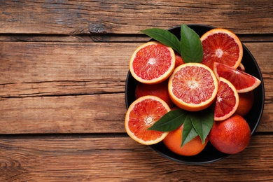 Photo of Whole and cut red oranges with green leaves on wooden table, top view. Space for text