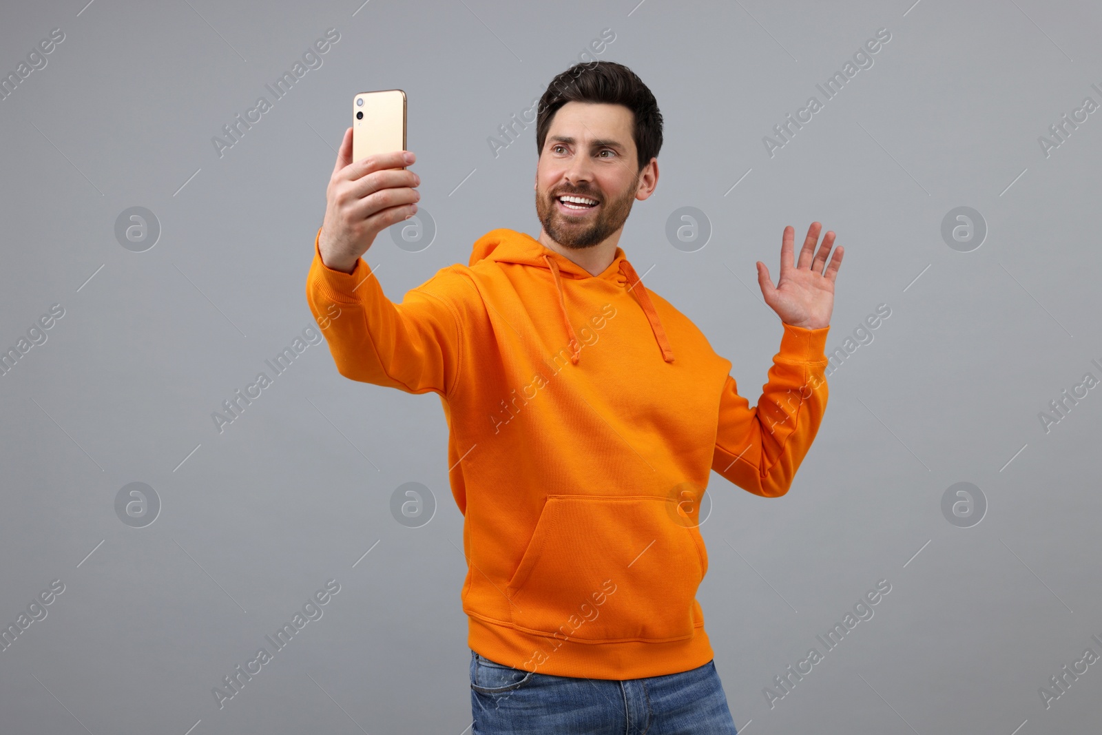 Photo of Smiling man taking selfie with smartphone on grey background, space for text