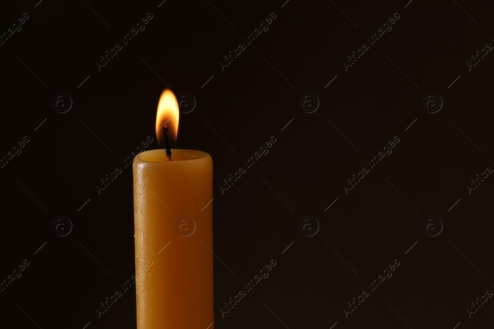 Photo of Burning church wax candle on dark background, space for text