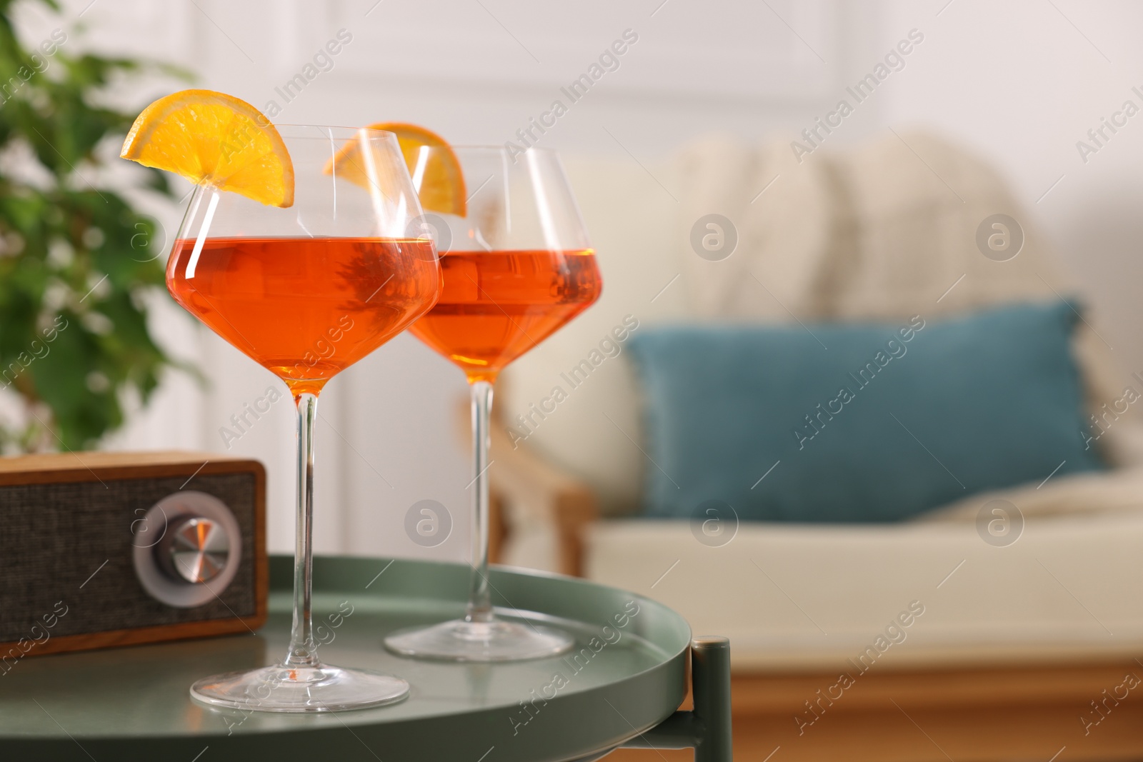 Photo of Tasty cocktail in glasses with orange slices and radio set on table in room, space for text. Relax at home