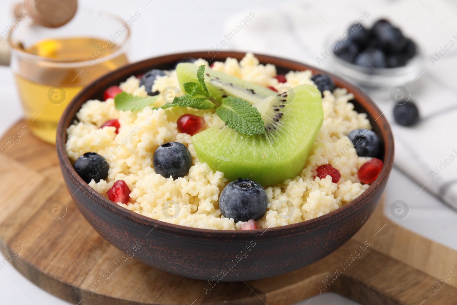 Photo of Bowl of tasty couscous with kiwi, blueberries and pomegranate on table, closeup