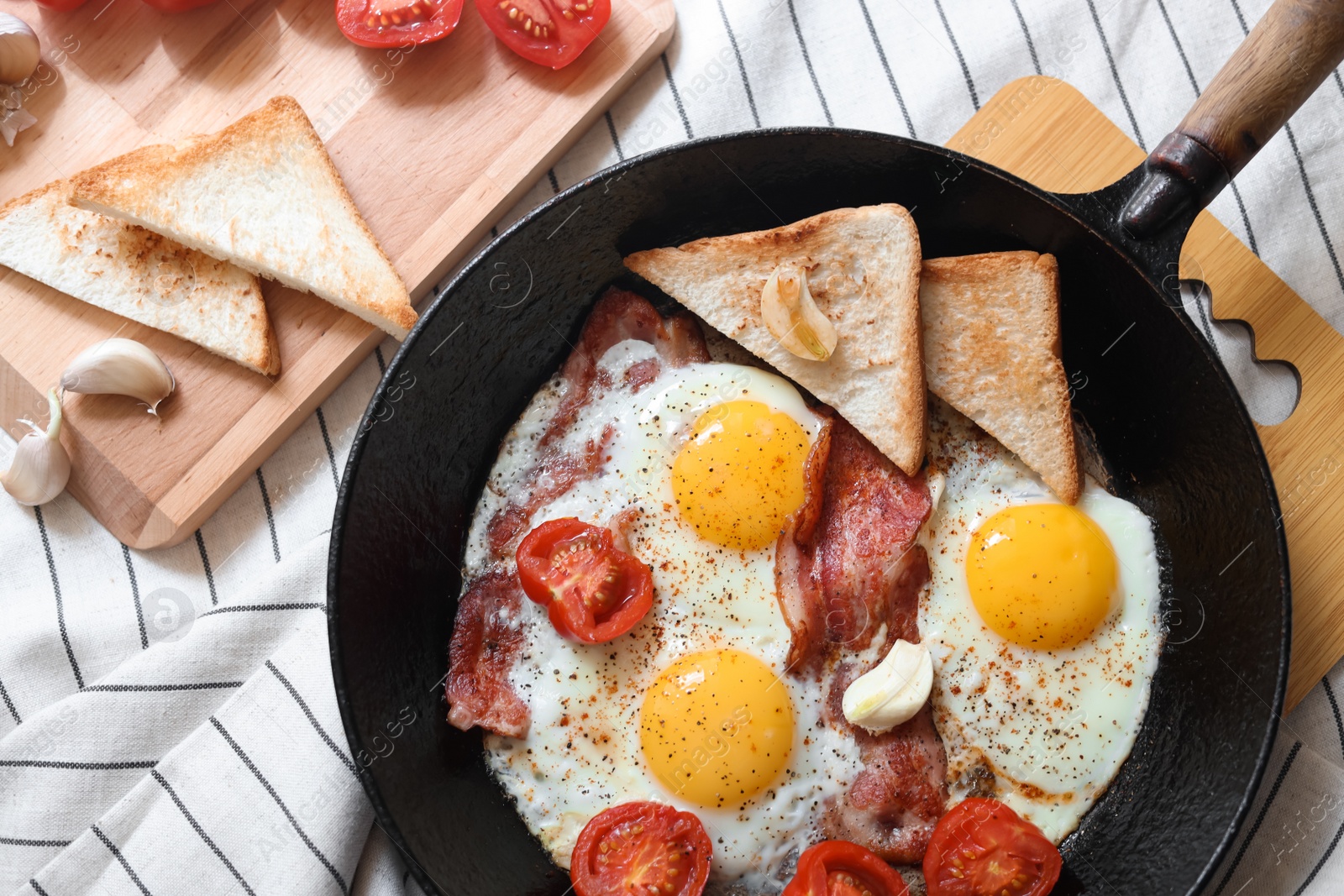 Photo of Delicious fried eggs with bacon and tomatoes in pan on table, flat lay