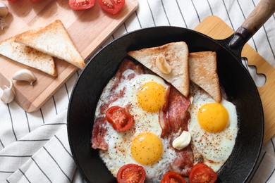 Delicious fried eggs with bacon and tomatoes in pan on table, flat lay