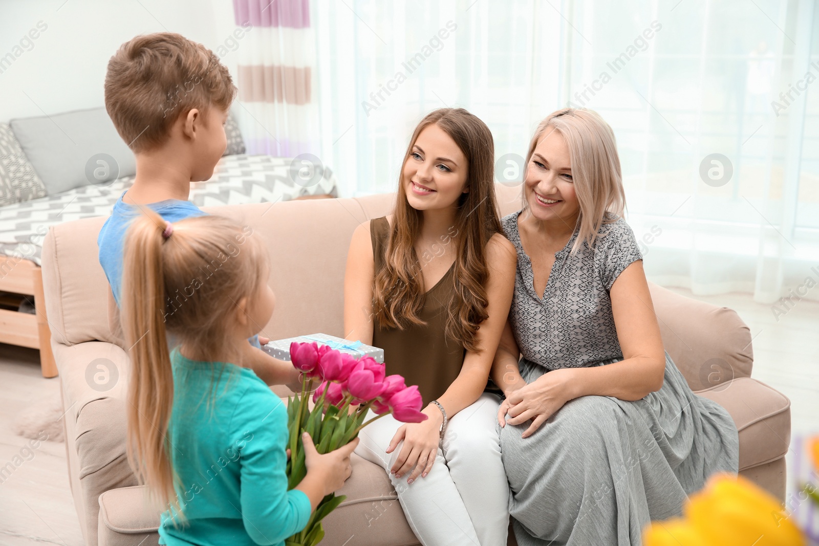 Photo of Cute little children congratulating mother and grandmother at home