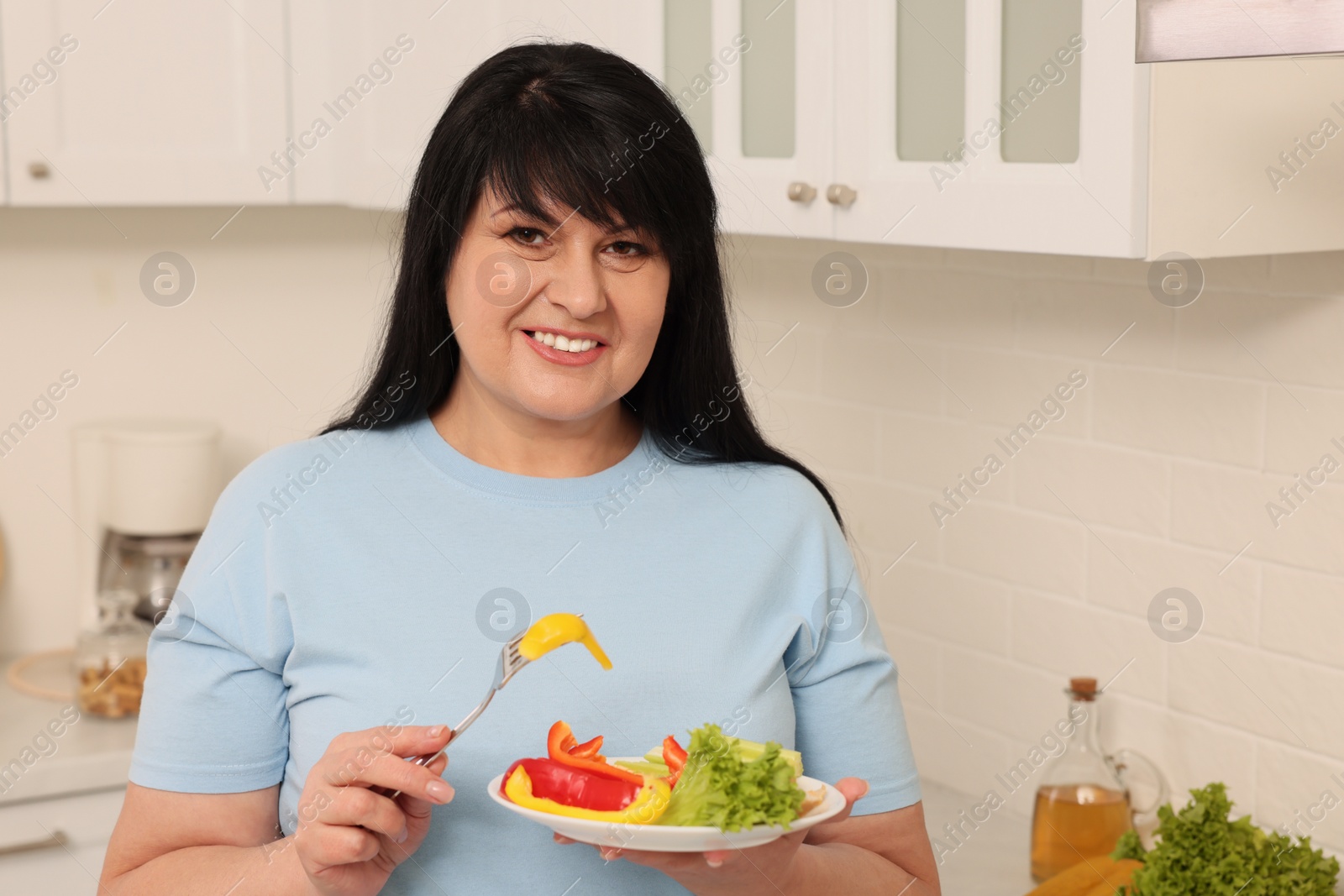 Photo of Happy overweight woman eating salad in kitchen. Healthy diet