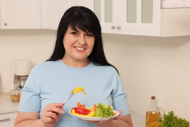 Happy overweight woman eating salad in kitchen. Healthy diet
