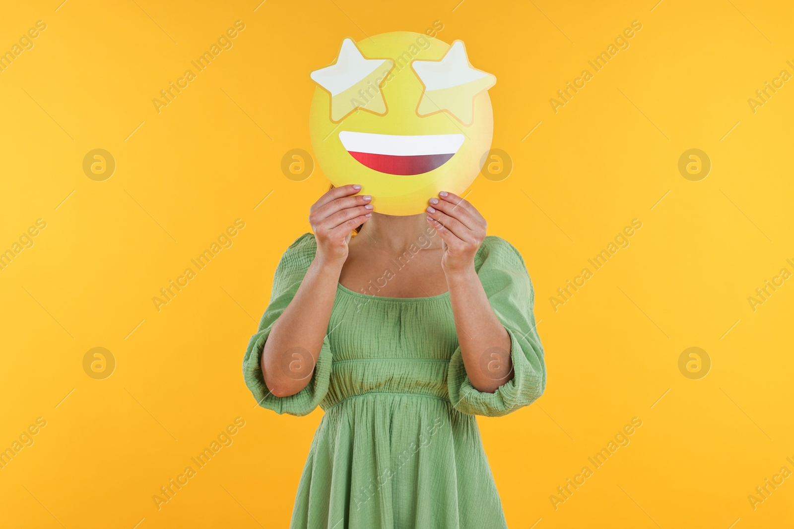 Photo of Woman holding emoticon with stars instead of eyes on yellow background