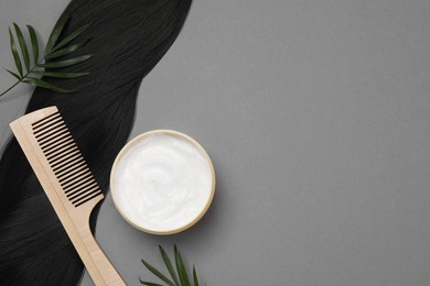 Lock of healthy black hair, comb and cosmetic product on grey background, flat lay. Space for text