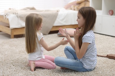 Photo of Cute little sisters playing clapping game with hands at home