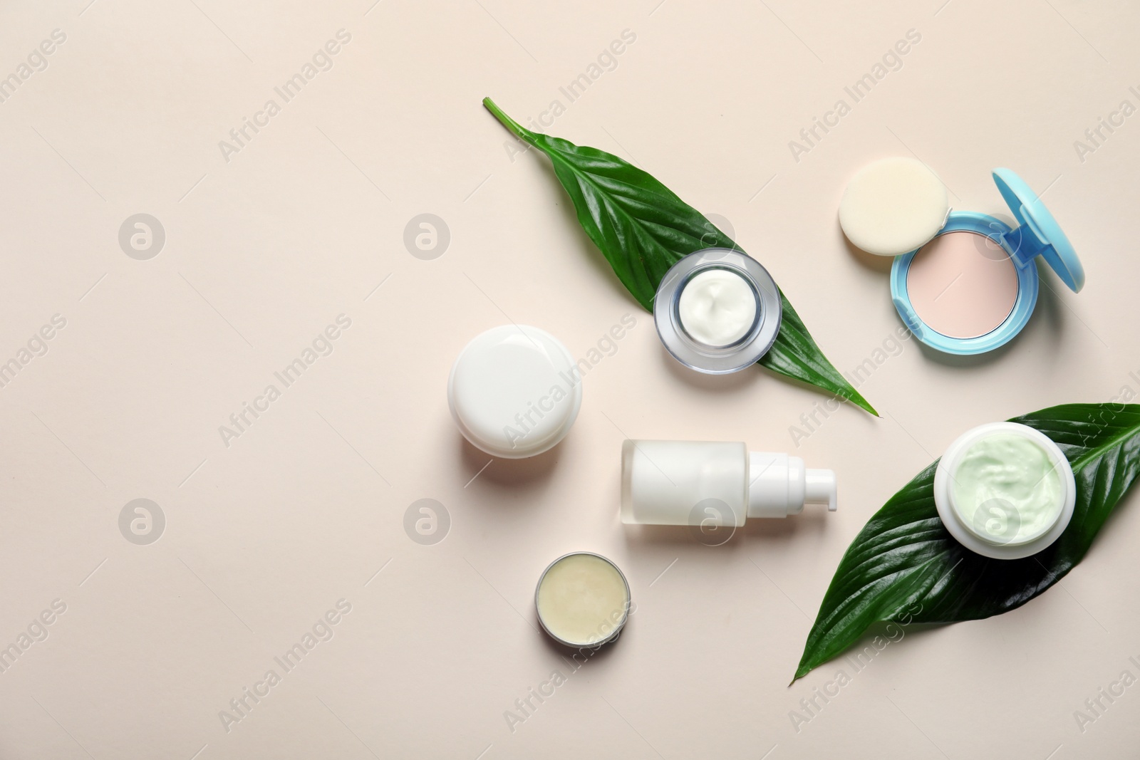Photo of Different skin care cosmetic products with green leaves on light background, top view