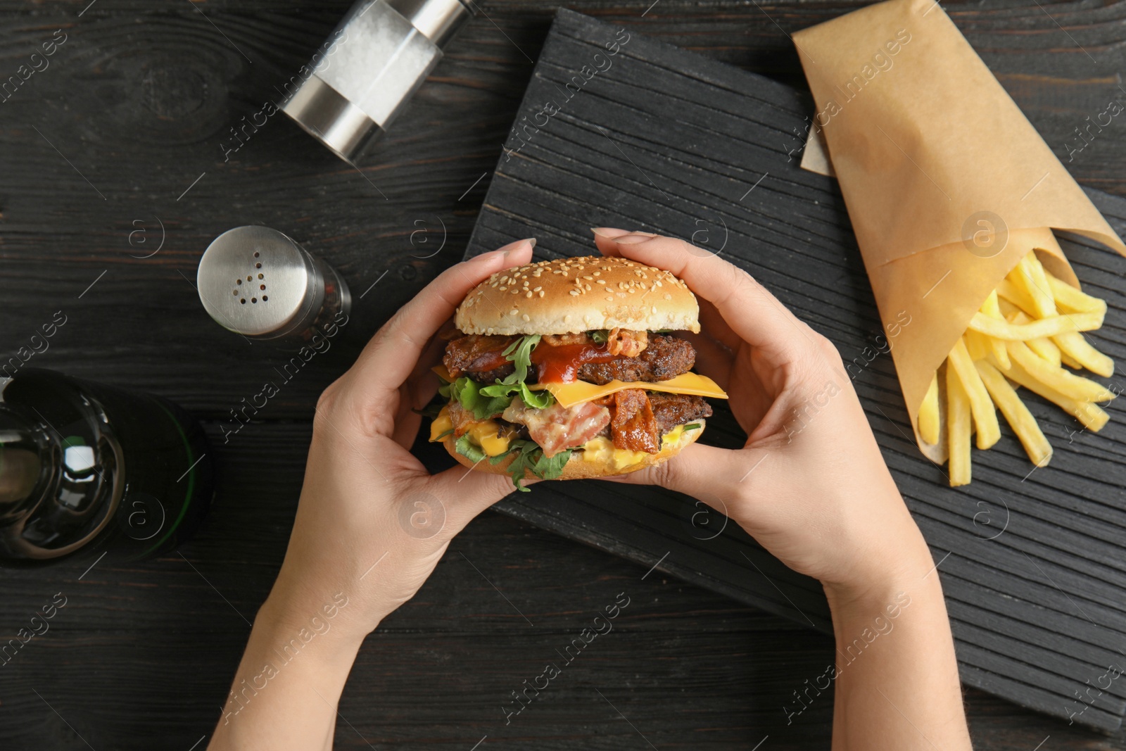 Photo of Woman holding burger with bacon at served table, top view