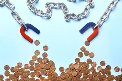 Photo of Chain with magnets attracting coins on light blue background, flat lay