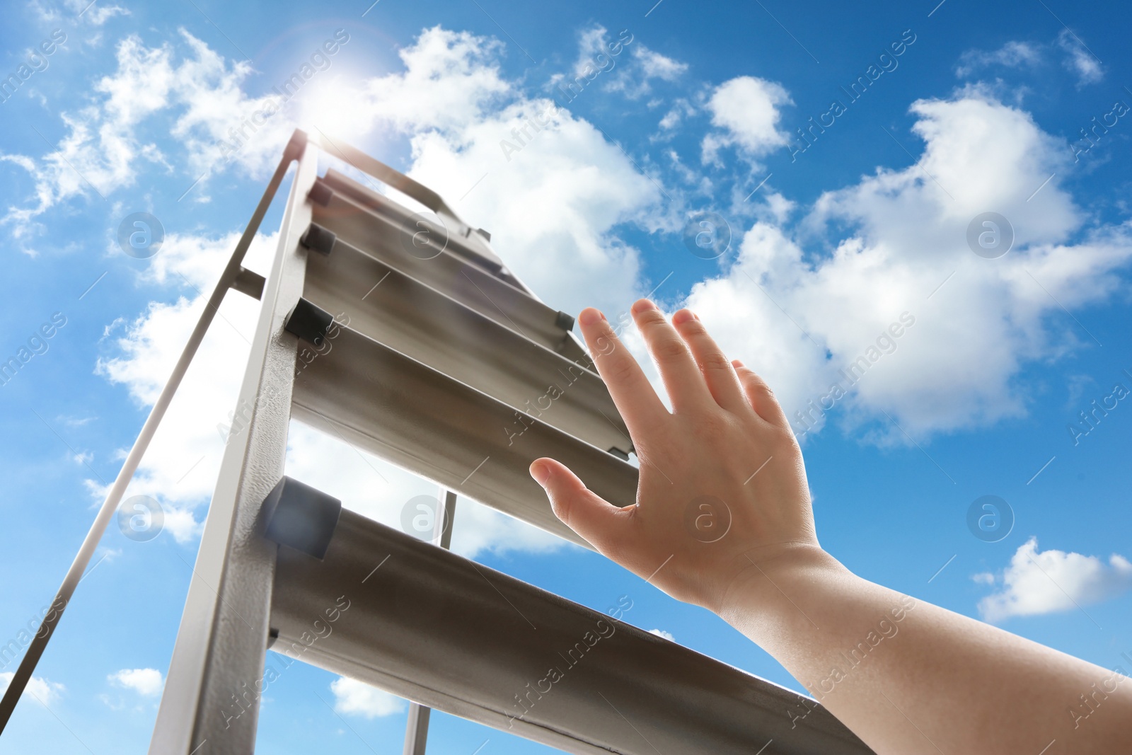 Image of Woman climbing up stepladder against blue sky with clouds, closeup