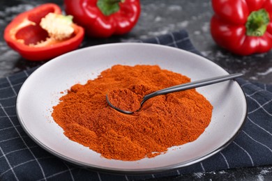 Photo of Plate of aromatic paprika and fresh peppers on black textured table, closeup