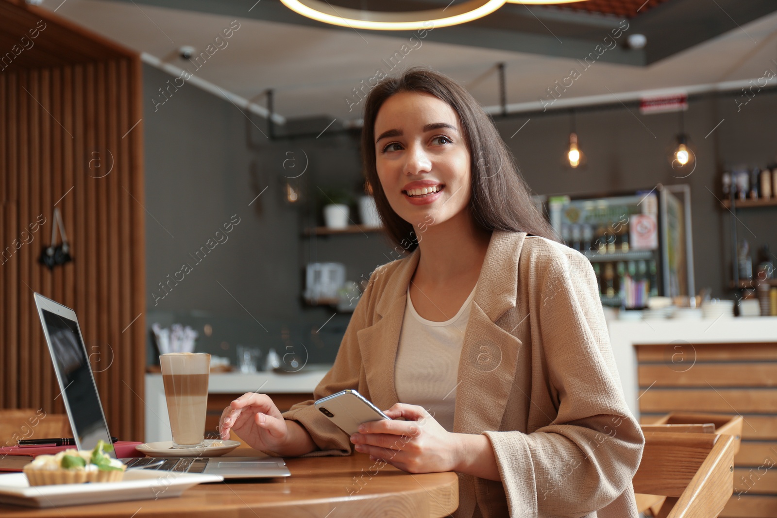 Photo of Young blogger with smartphone and laptop in cafe