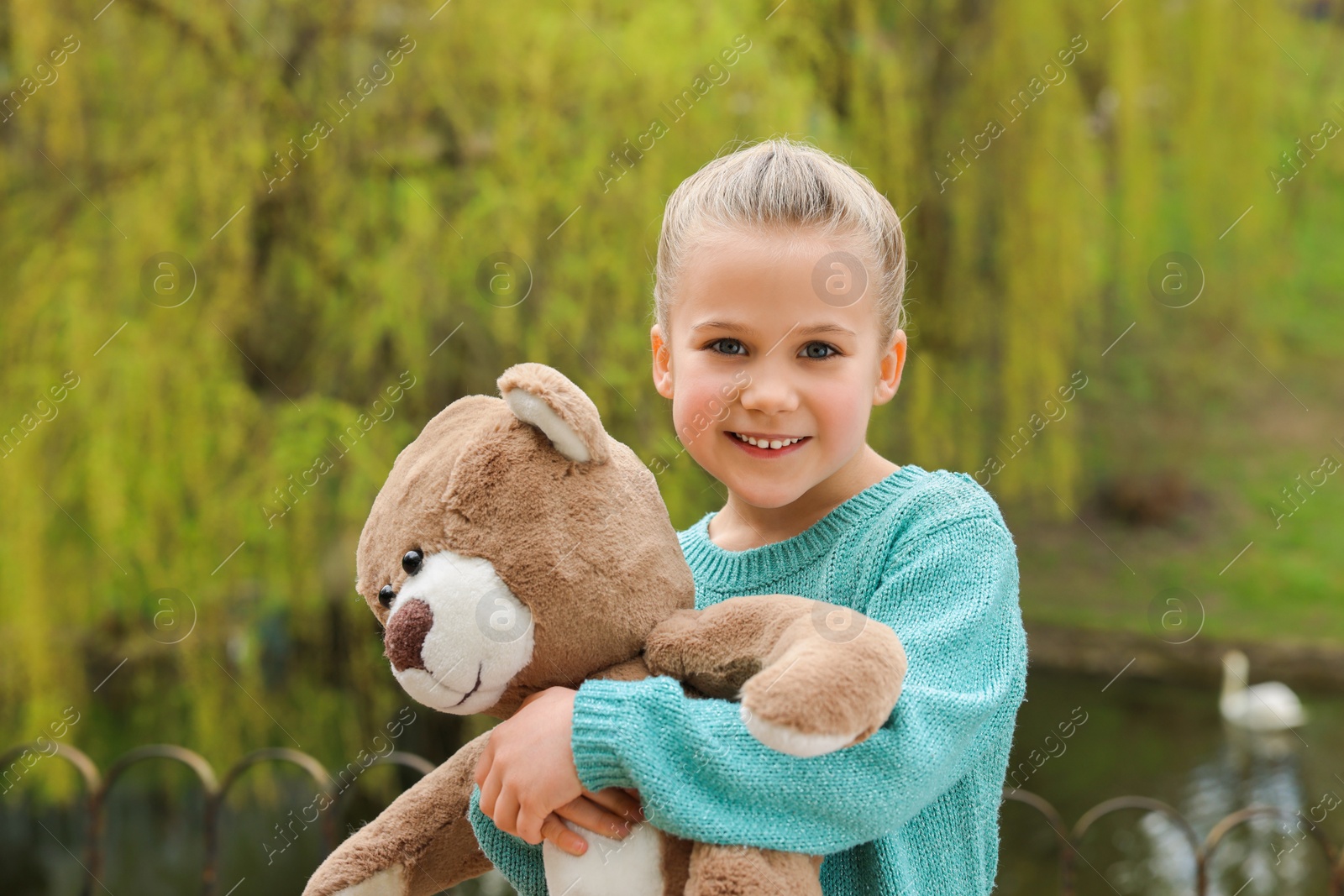 Photo of Cute little girl with teddy bear outdoors