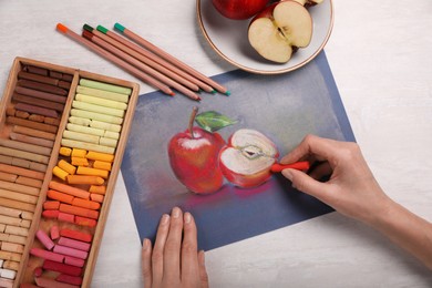 Photo of Woman drawing apples on paper with soft pastels at white table, top view