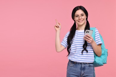Photo of Smiling student with smartphone and backpack pointing at something on pink background. Space for text