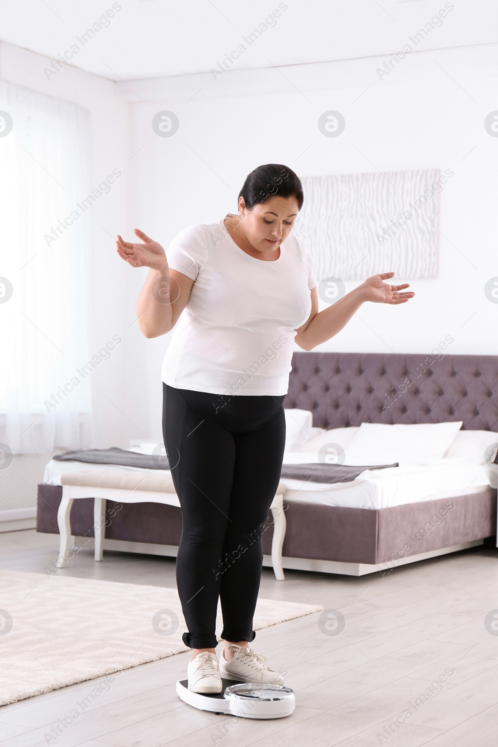 Photo of Overweight woman in sportswear using scales in bedroom