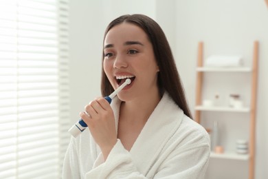 Photo of Young woman brushing her teeth with electric toothbrush in bathroom