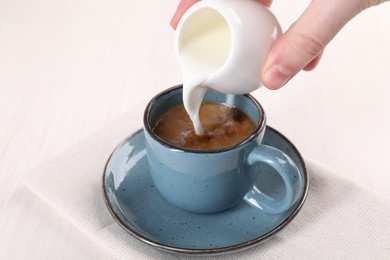 Woman pouring milk into cup with aromatic coffee at white wooden table, closeup