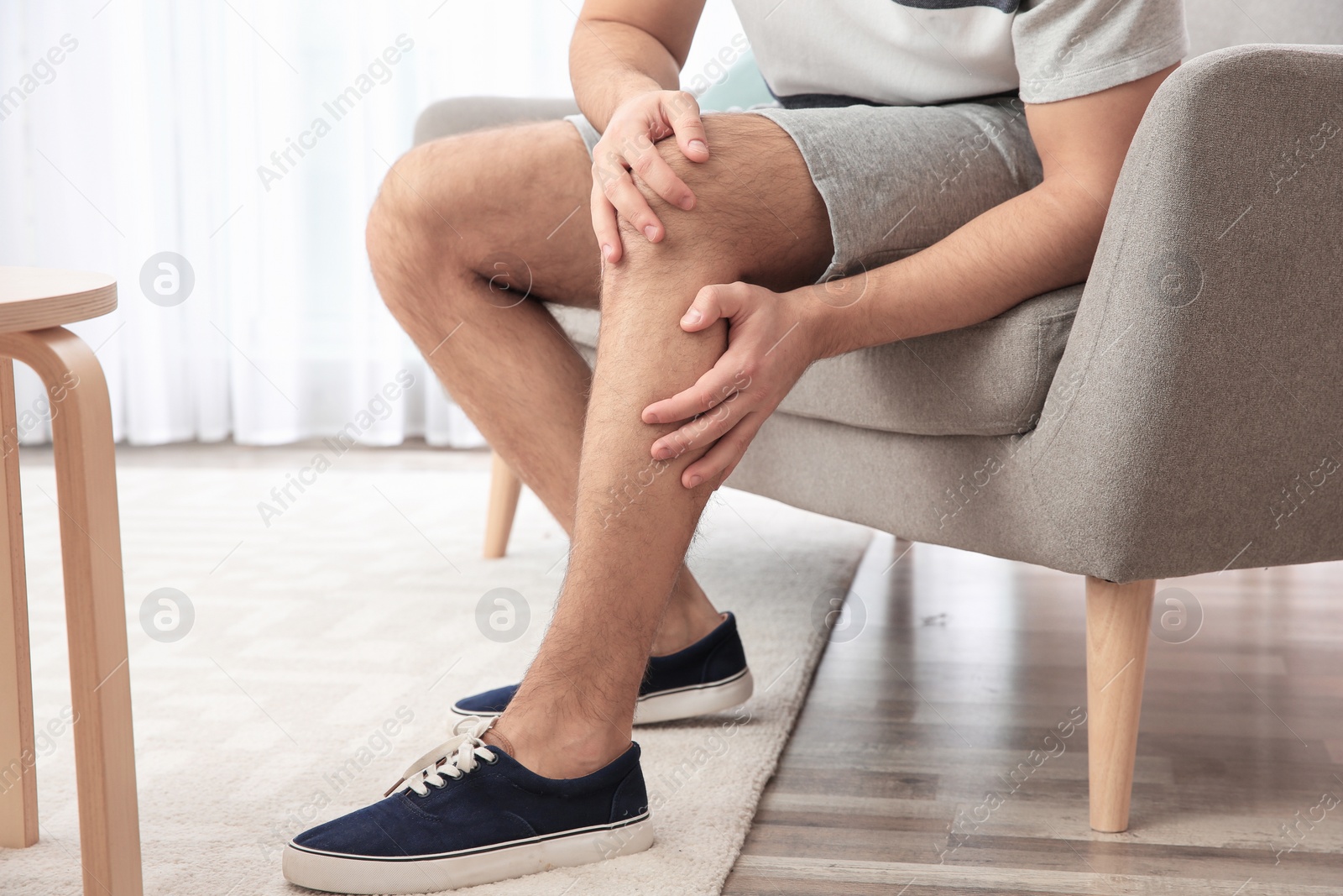 Photo of Man suffering from leg pain at home, closeup