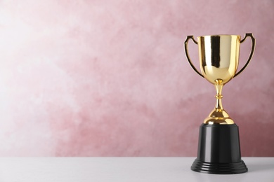 Golden trophy cup on table against pink background. Space for text