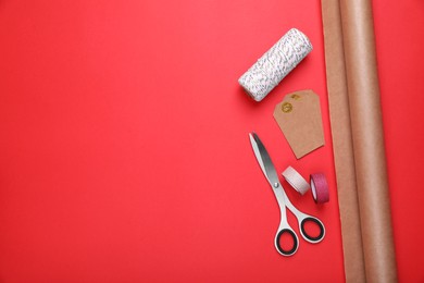 Photo of Roll of wrapping paper, scissors, tags and ribbons on red background, flat lay. Space for text