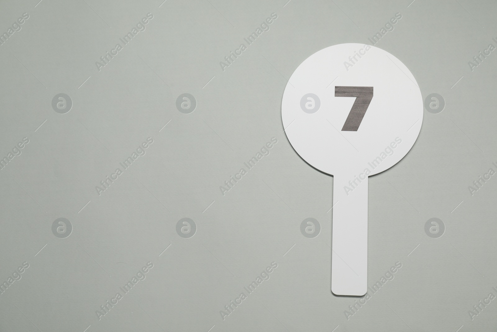Photo of Auction paddle with number 7 on light grey background, top view. Space for text